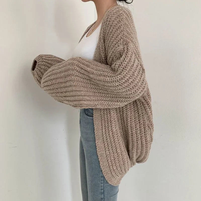 Person wearing a beige chunky knit sweater against a plain background