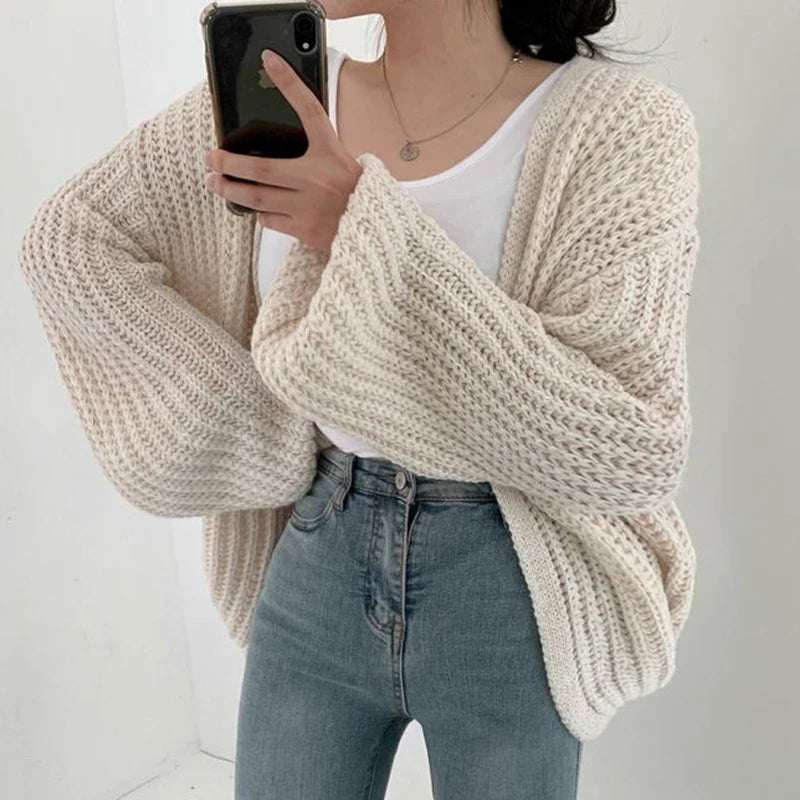 Person wearing a beige chunky knit sweater and blue jeans, holding a phone.