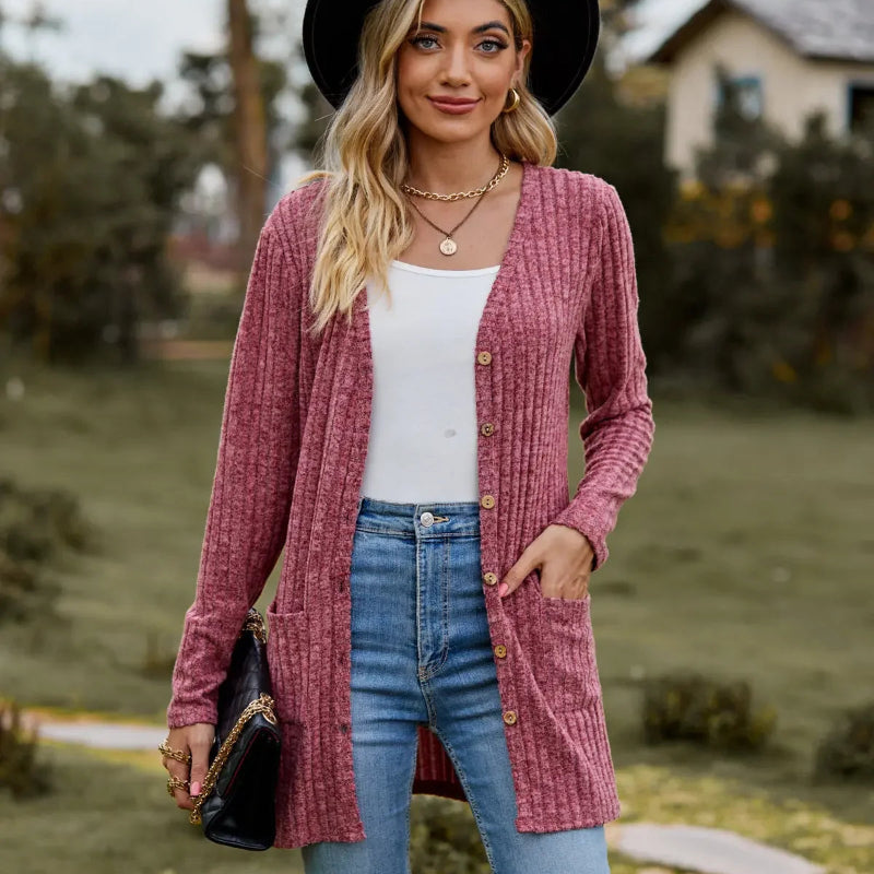 Woman wearing a pink cardigan, white top, and blue jeans outdoors.