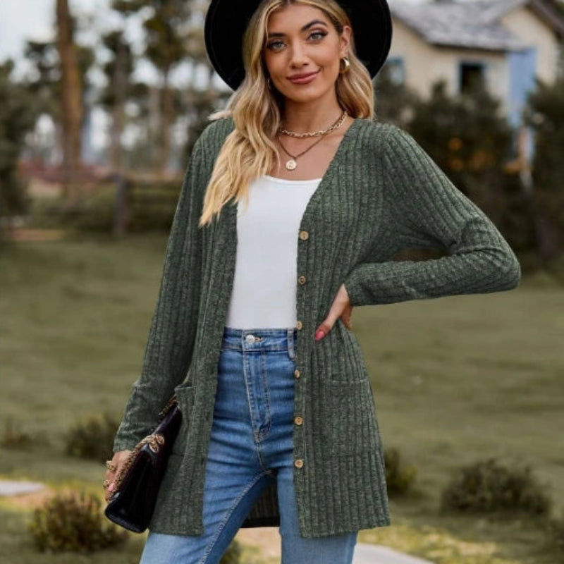Woman wearing a green cardigan, white top, and blue jeans outdoors.
