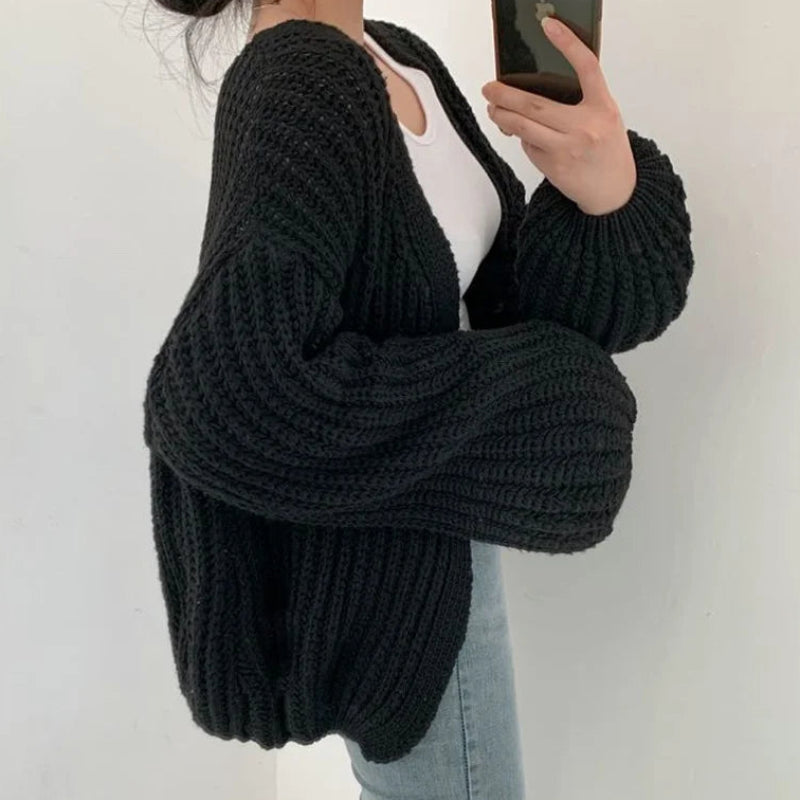 Person wearing a black chunky knit cardigan against a white background