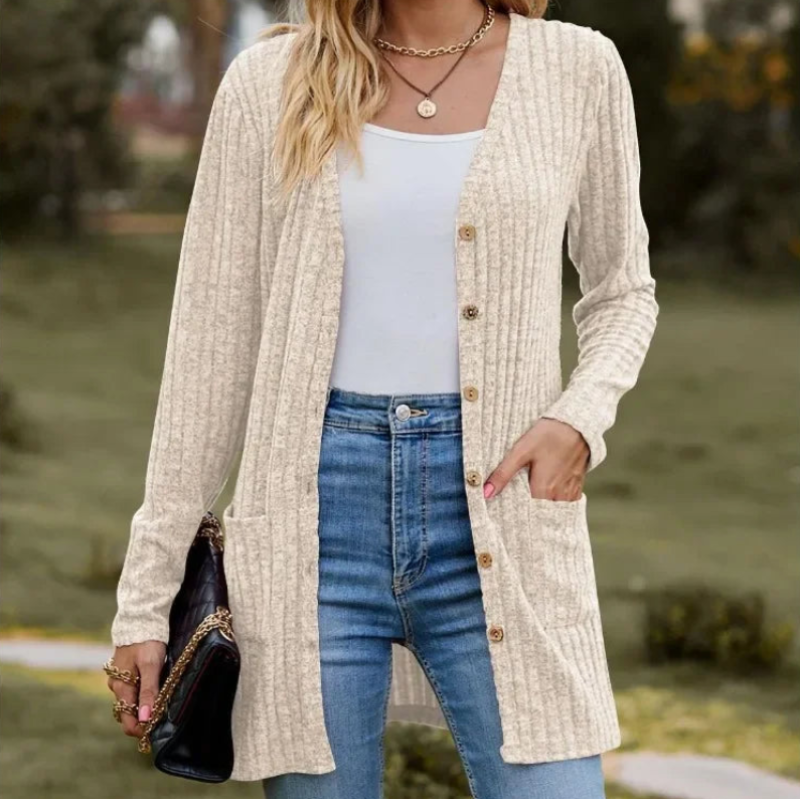 Woman wearing a beige cardigan, white top, and blue jeans outdoors.